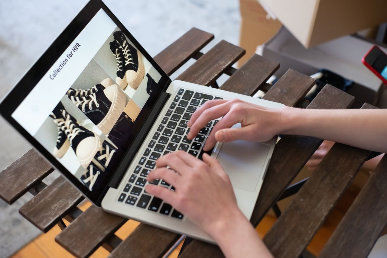 brand-01 A person’s hands are browsing the HER collection on an online shoe shop with a laptop.